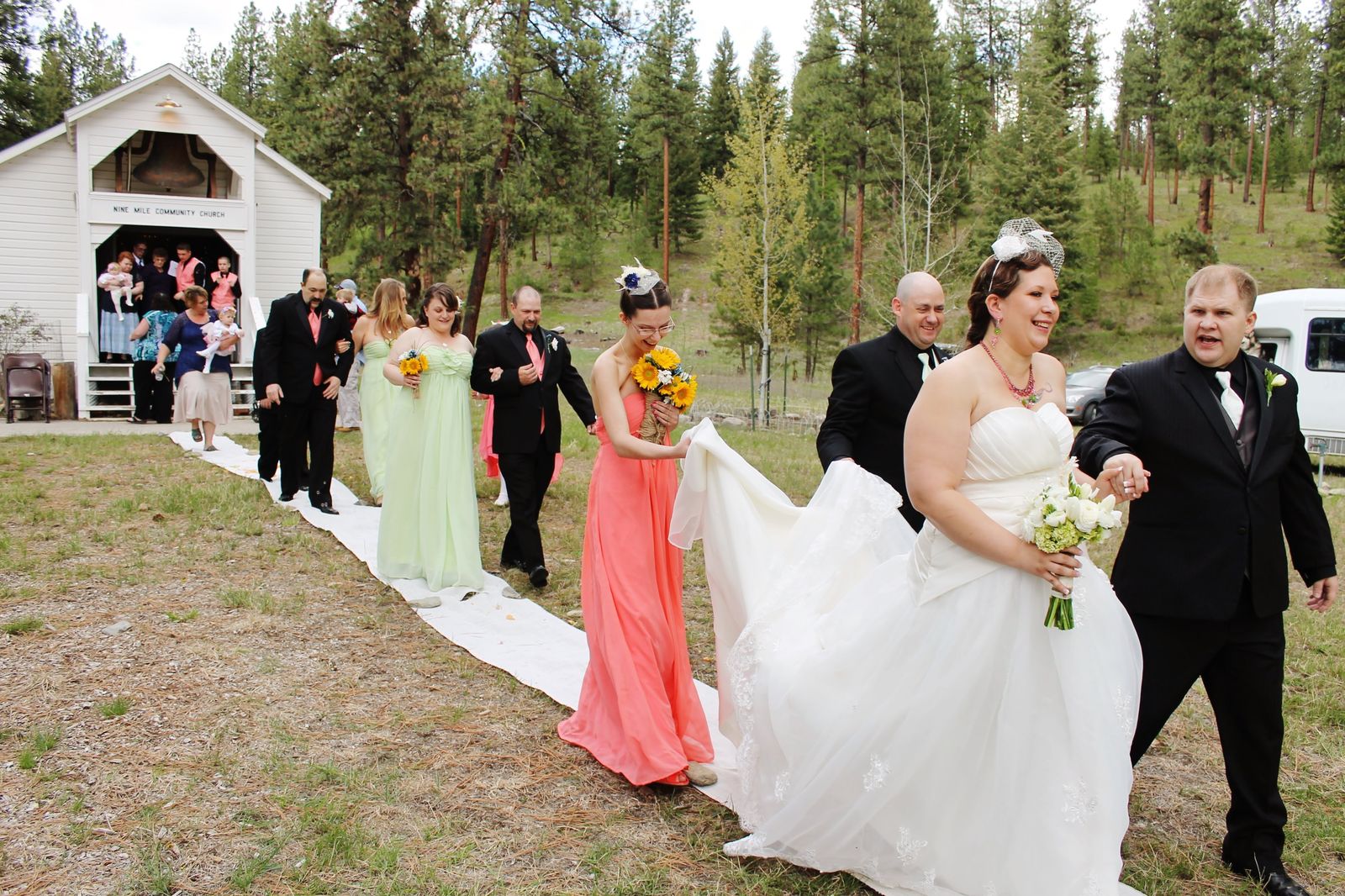 Wedding party walking down an outdoor aisle toward a white chapel