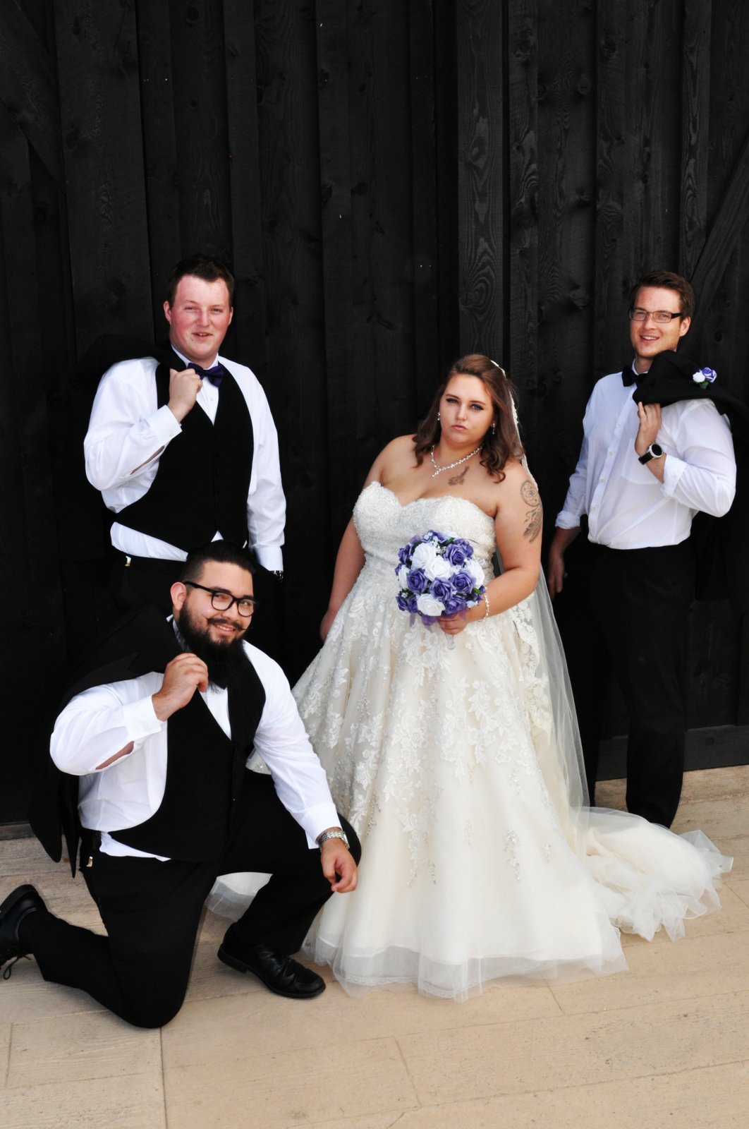 Bride with groomsmen against black barn wall